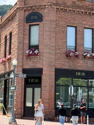 Downtown Aspen pedestrian mall with colorful overhead banners, trees, storefronts, and visitors