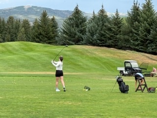 Golfer on a mountain course with evergreen trees and Aspen peaks in the background
