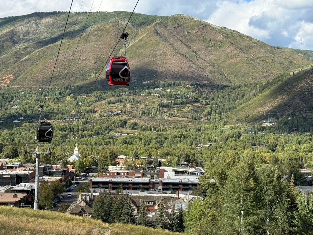 Aspen gondola cabins above downtown Aspen with green mountains in the background